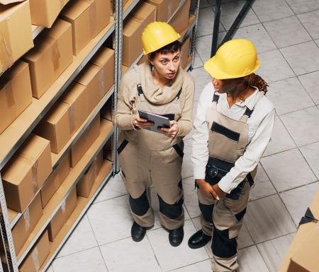 two women overalls working with industrial goods planning shipment products with digital tablet team employees doing inventory storage room manufacturing products